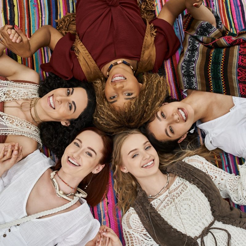top view of cheerful interracial women looking at camera on blanket in retreat center